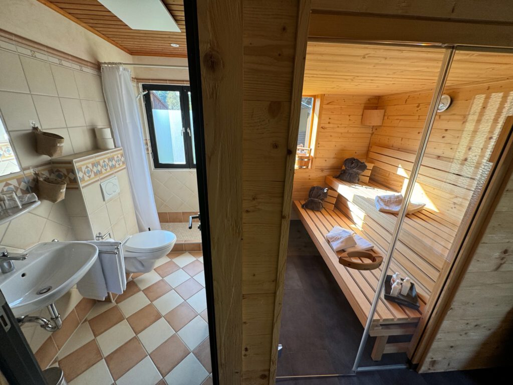 Badezimmer mit Blick durch eine offene Tür auf eine hölzerne Sauna