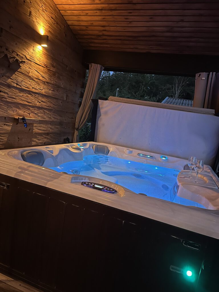 Beleuchteter Whirlpool mit blauem Licht und zwei Weingläsern am Abend