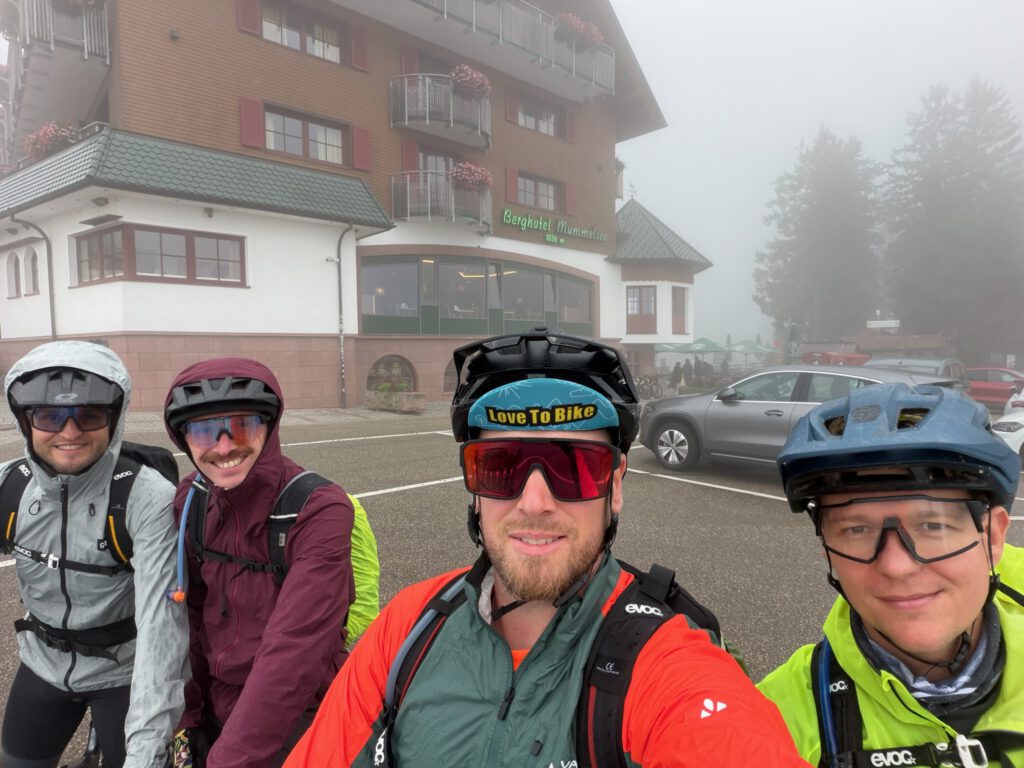 Vier Radfahrer in Regenkleidung vor dem nebelverhangenen Berghotel Mummelsee