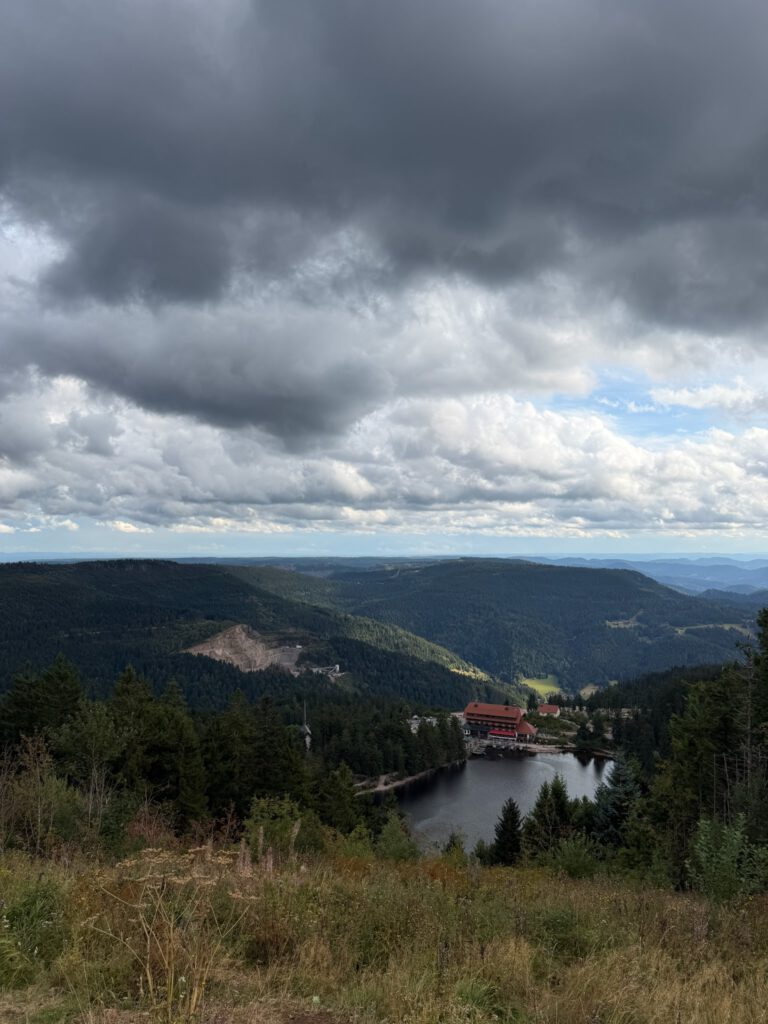 Blick von oben auf den Mummelsee mit dem Berghotel am Ufer, umgeben von dichten Wäldern