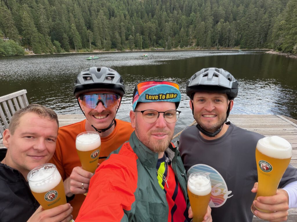 Vier Personen stoßen mit Weizenbier am Mummelsee an, im Hintergrund Tretboote